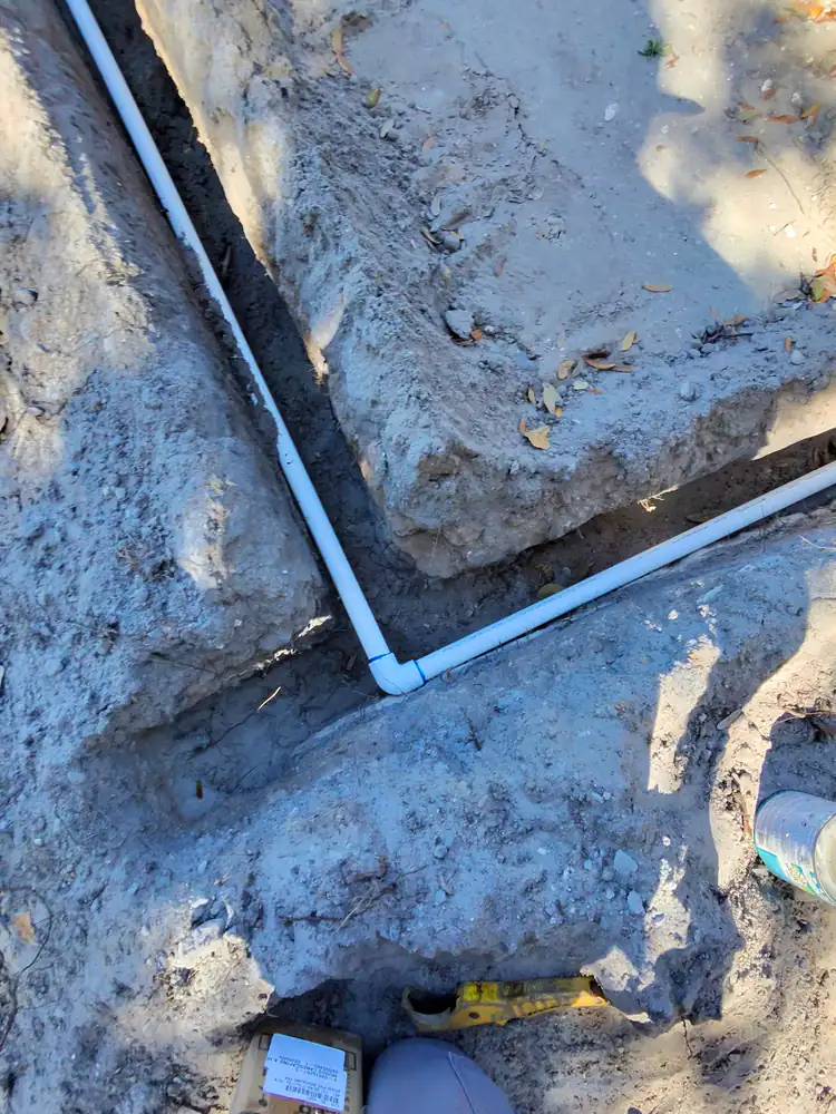 White PVC irrigation pipe with an elbow fitting laid in an open dirt trench