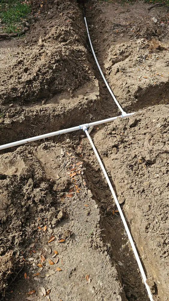 White PVC irrigation pipes and tee fittings laid in freshly dug trenches