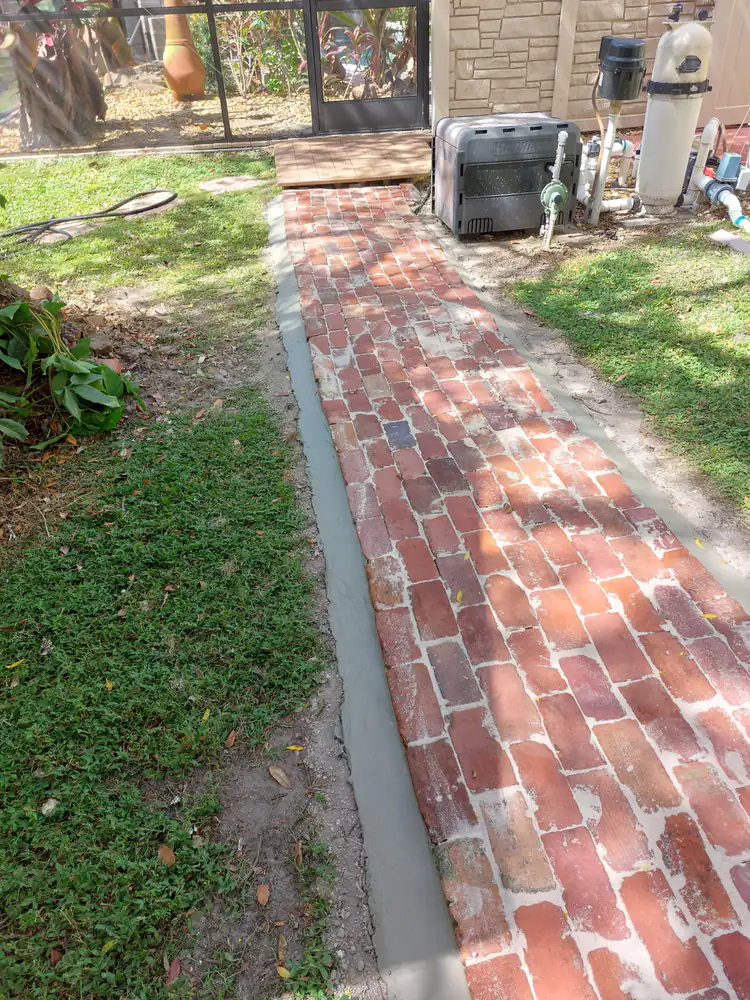 A new reclaimed-brick walkway with fresh concrete edging beside pool equipment