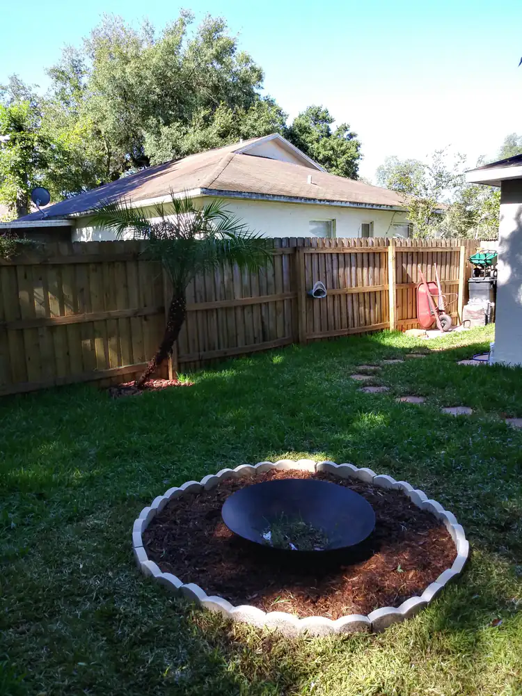 A backyard fire-pit bowl in a scalloped-edge mulch circle on a new lawn