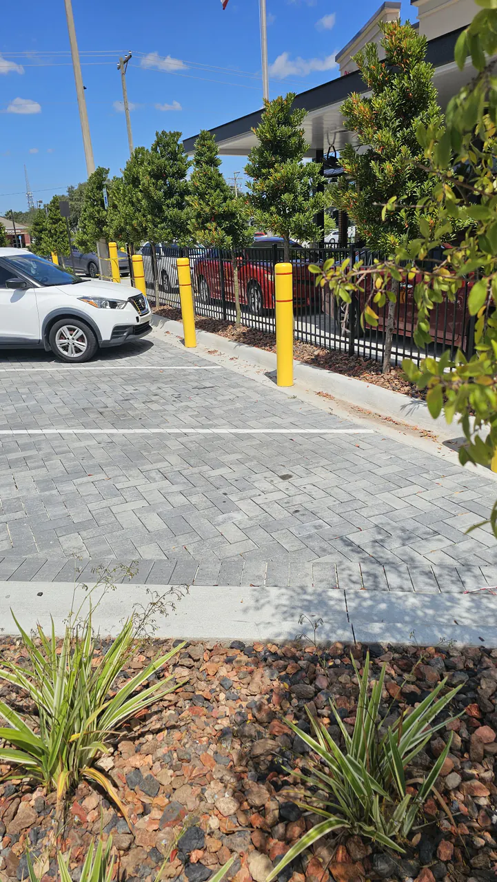 A finished gray herringbone paver parking pad bordered by rock beds and yellow bollards