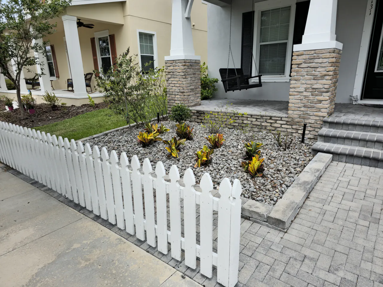 Yellow and red crotons freshly planted in the gravel bed by the white picket fence