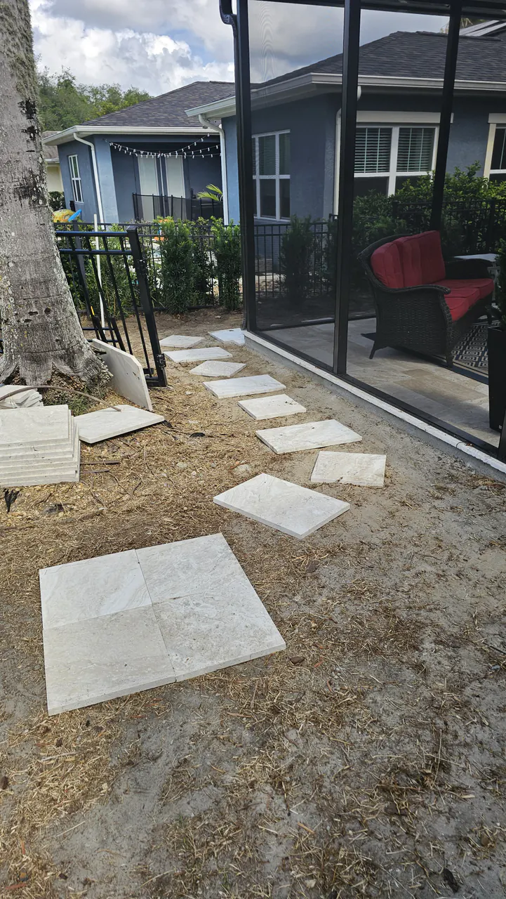 Travertine paver slabs arranged loose on bare ground beside a screened patio