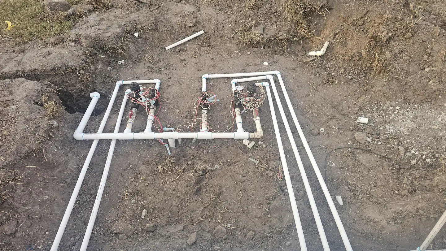 A newly assembled irrigation valve manifold with wired solenoids and PVC supply lines laid in an open trench