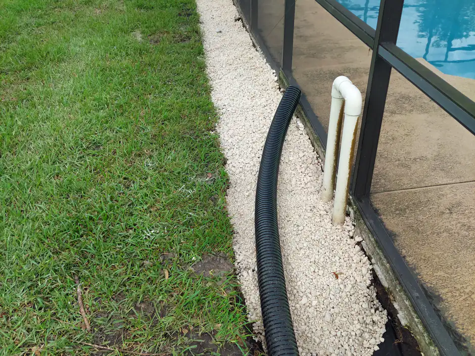 A French-drain gravel bed and corrugated drain pipe Woods installed along a pool screen enclosure to move water off the yard