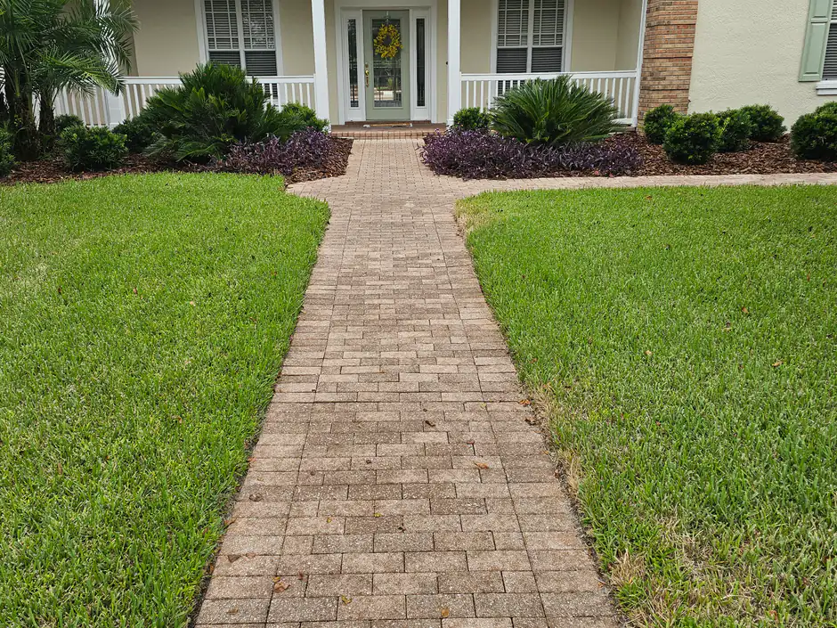 A healthy, edged Florida lawn on both sides of a paver walkway leading to a front porch